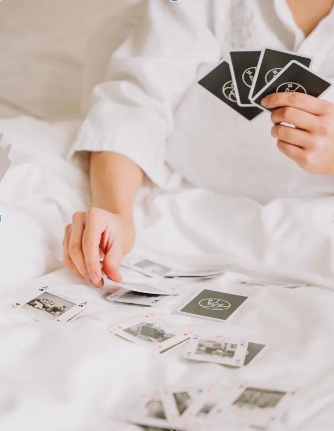 Gäst i hotellrock spelar med Hôtel Reisens kortlek i sängen, mörkgröna baksidor med hotellets monogram